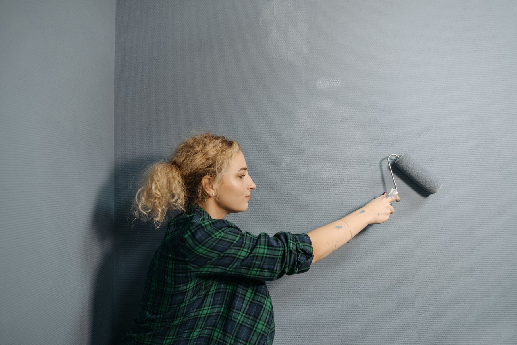 Malerin streicht Innenwand mit der Rolle